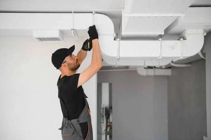 Technician inspecting white overhead ventilation ductwork