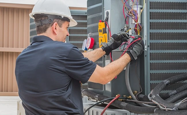 Technician in a white hard hat testing an outdoor HVAC unit